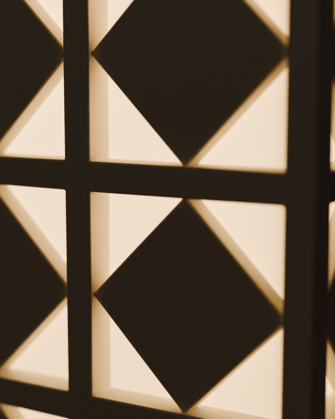 Close-up of the ANGIN cordless lamp in bone white, switched on, against a breeze-block wall, diamond cells, four lit triangles each