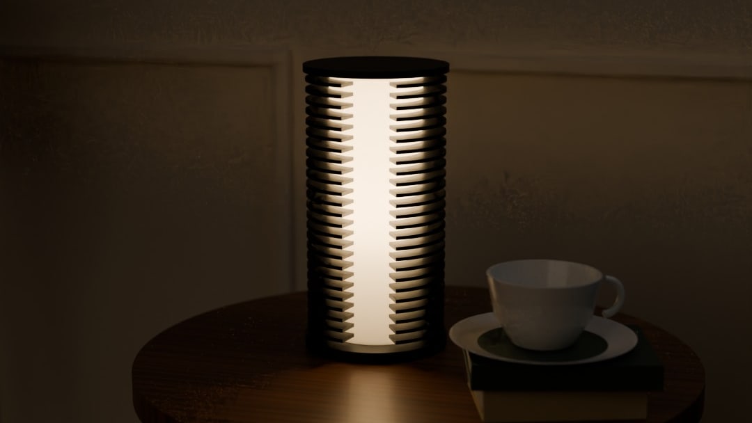 COLUMN table lamp in graphite, switched on, on a round wooden side table beside a teacup and books at night