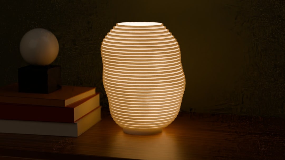 KONTUR table lamp in bone white, switched on, on a teak sideboard beside art books at night