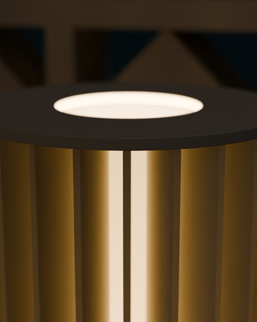 Close-up of the SIRIP table lamp in bone white, switched on, against a breeze-block wall, fin edges glowing at the top ring