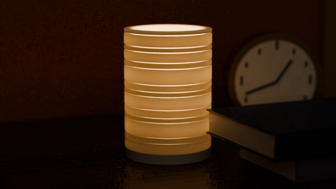 TERAS cordless lamp in bone white, switched on, on a walnut nightstand beside a clock and books at night