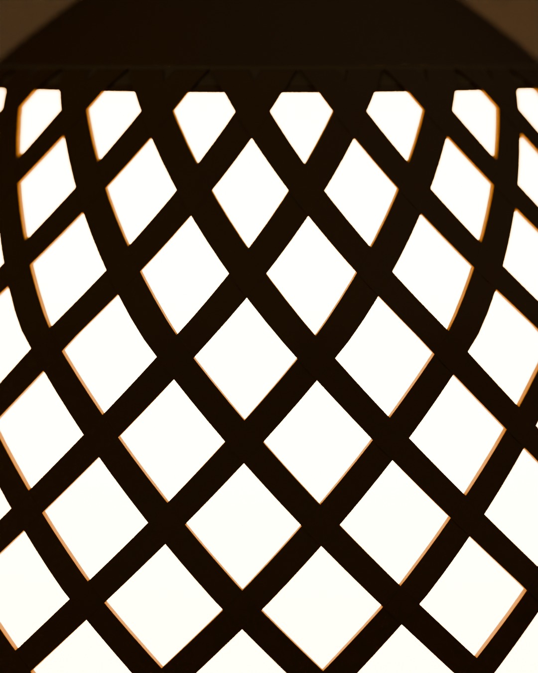 Close-up of the TUDUNG table lamp in bone, red and brass, switched on, in a Hari Raya living room, light through the woven diamonds